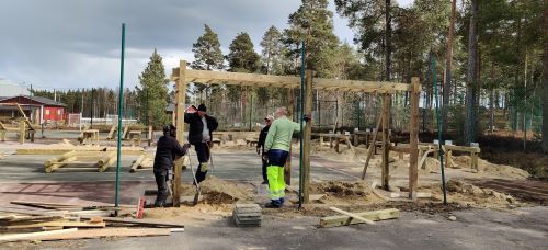 Fyra personer vid monkey-baren, en person str nere i en av groparna och hller i en spade, tv av personerna lutar sig mot monkey-baren. Material (tr) ligger utspritt p marken.